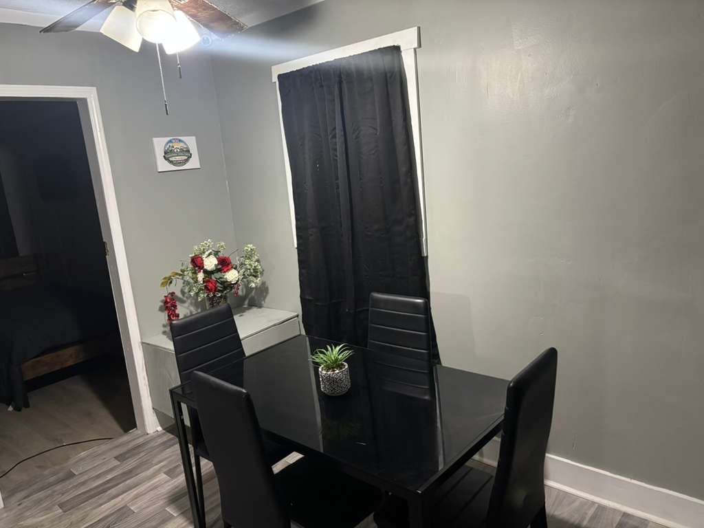 Black glass dining table and chairs in a gray room with black curtains and flowers.