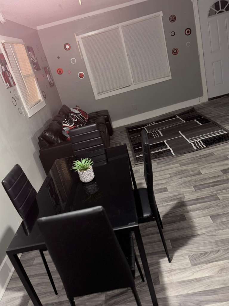 Modern grey living space with black glass dining table, leather sofa, and patterned area rug.