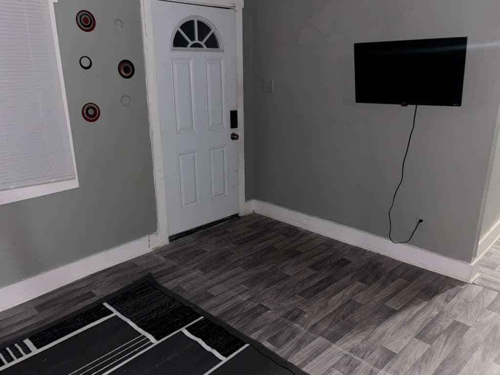 Grey room with wood-look flooring, a white front door, and a wall-mounted television.