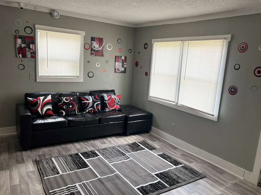 Modern gray living room with black leather sofa, red accents, and geometric area rug.