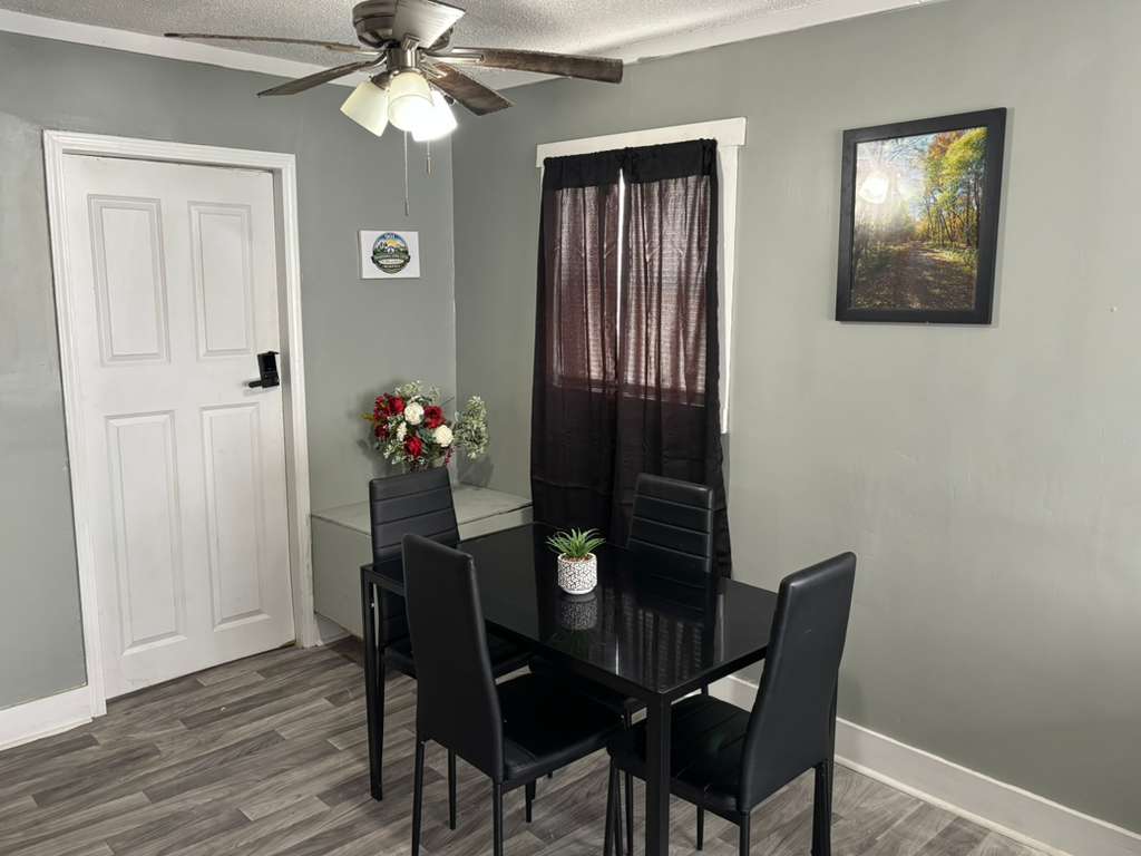 Black dining set in a gray room with a white door and ceiling fan.